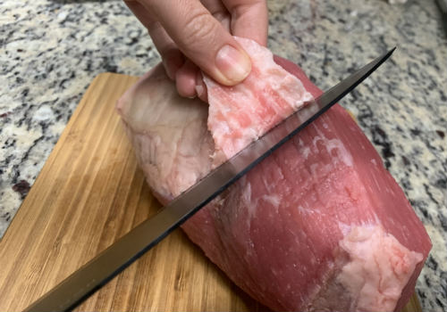Knife trimming a strip of fat from an eye of round roast