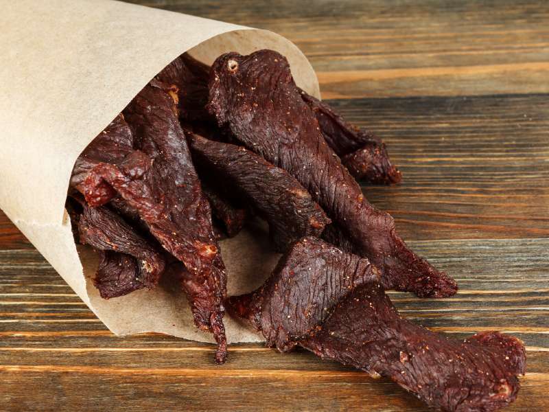 Beef jerky strips spilling from a paper cone onto a wooden table