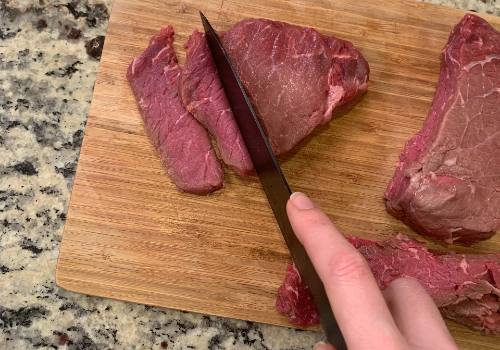 A knife cutting firm beef into long, thin slices
