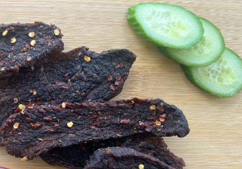 Pepper-speckled beef jerky beside cucumber slices