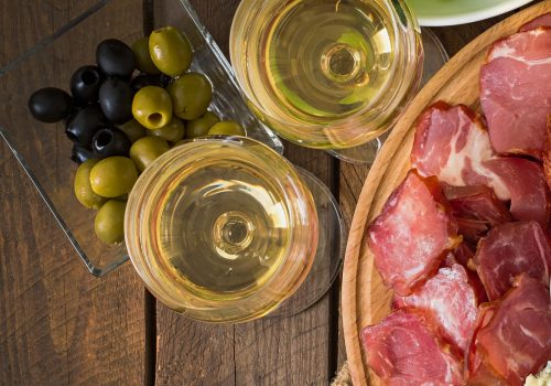 Glasses of white wine beside olives and sliced cured meat