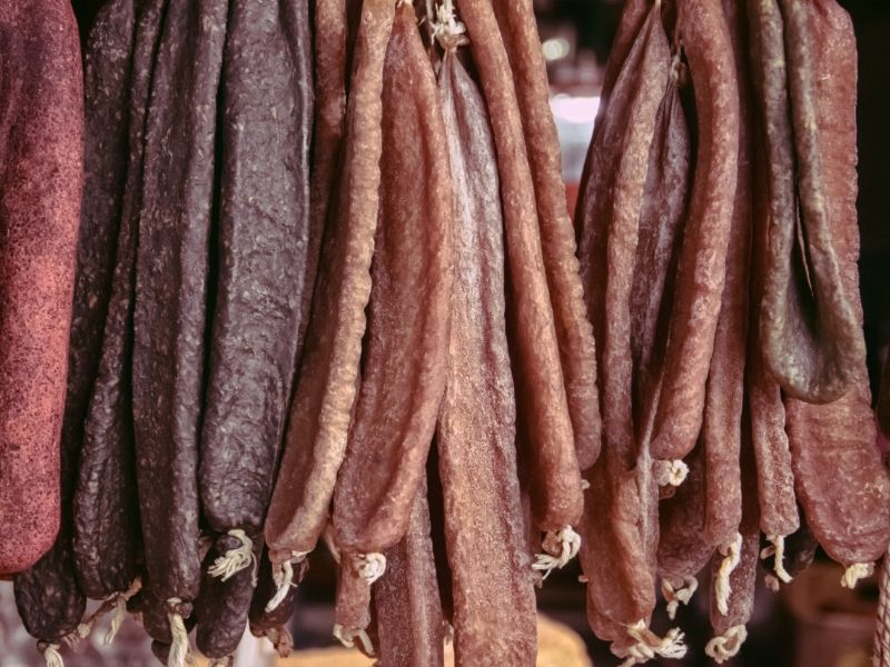 Rows of dried sausages and long strips of meat hanging at a market