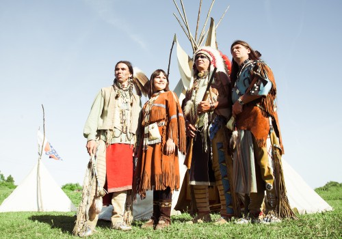 Four people in traditional dress standing beside a tipi