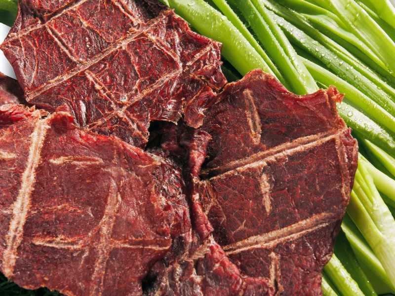 Slices of dried beef arranged beside green vegetables