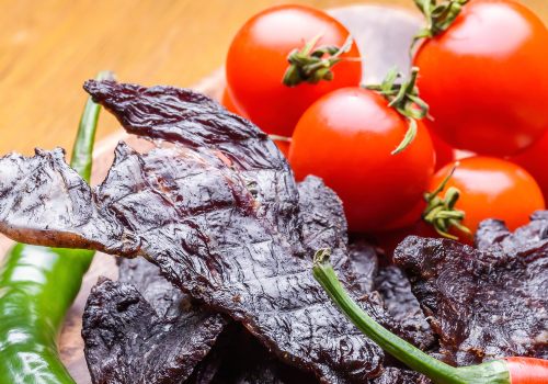 Dark beef jerky strips beside tomatoes and greens