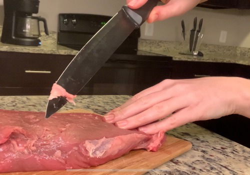 A cook trimming fat from raw beef with a knife