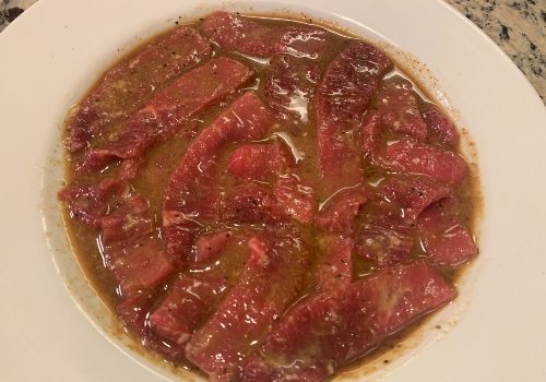 Beef strips submerged in brown sugar marinade in a bowl