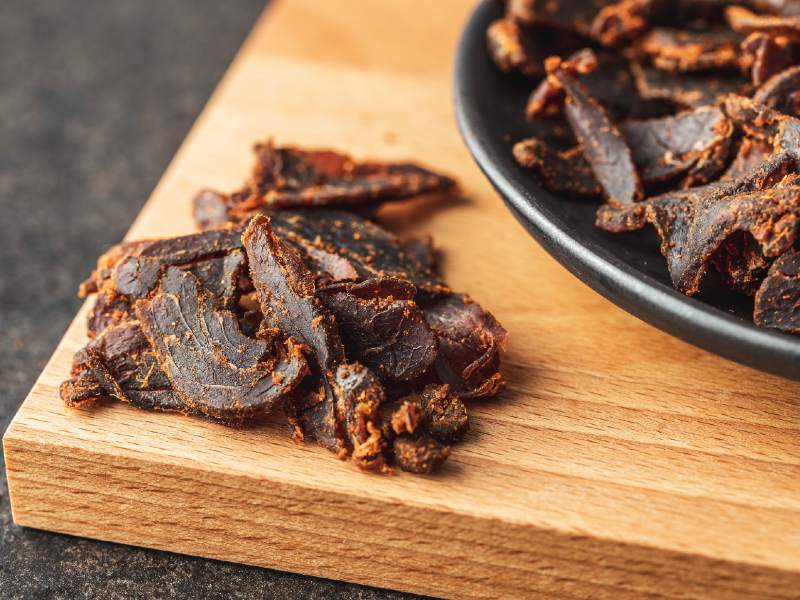 Curled beef jerky pieces on a board beside a dark plate