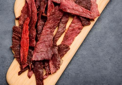 Long red-brown jerky strips arranged on a wooden board