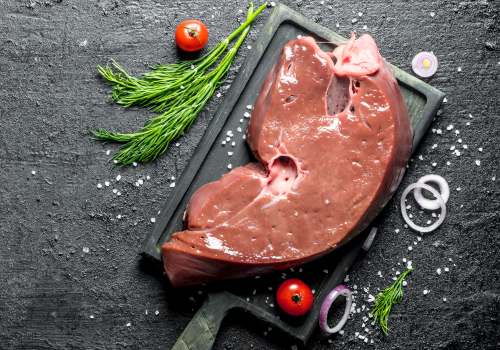 Raw liver on a dark board with herbs and vegetables