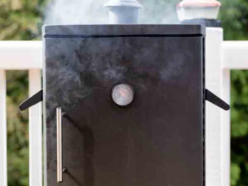 An upright outdoor smoker releasing smoke from the top