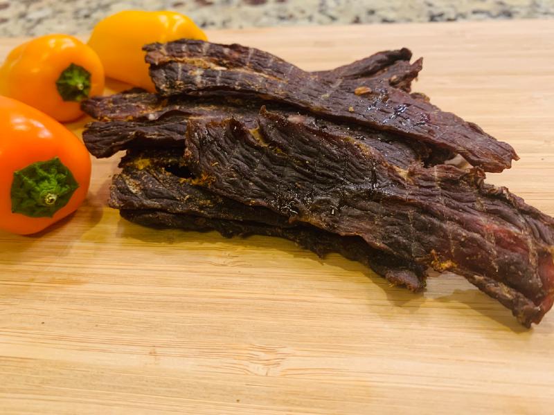 Homemade beef jerky strips beside orange habanero peppers