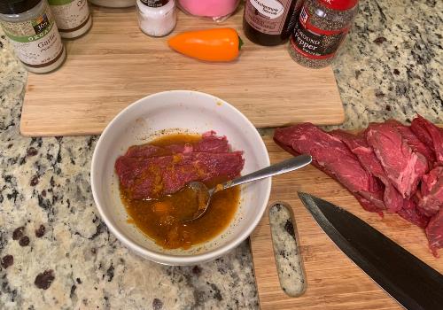 A beef slice being coated in marinade beside habaneros and seasonings