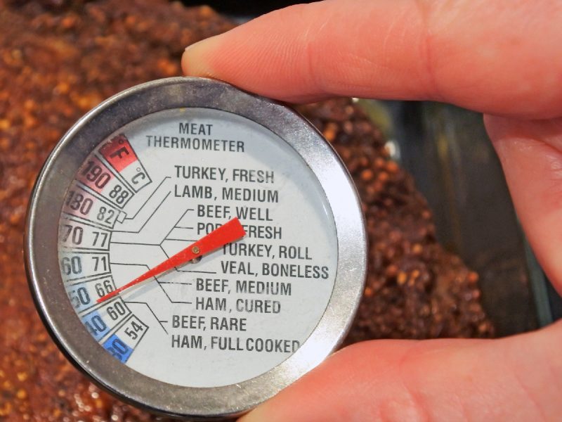 A hand checking a dial meat thermometer in cooked meat