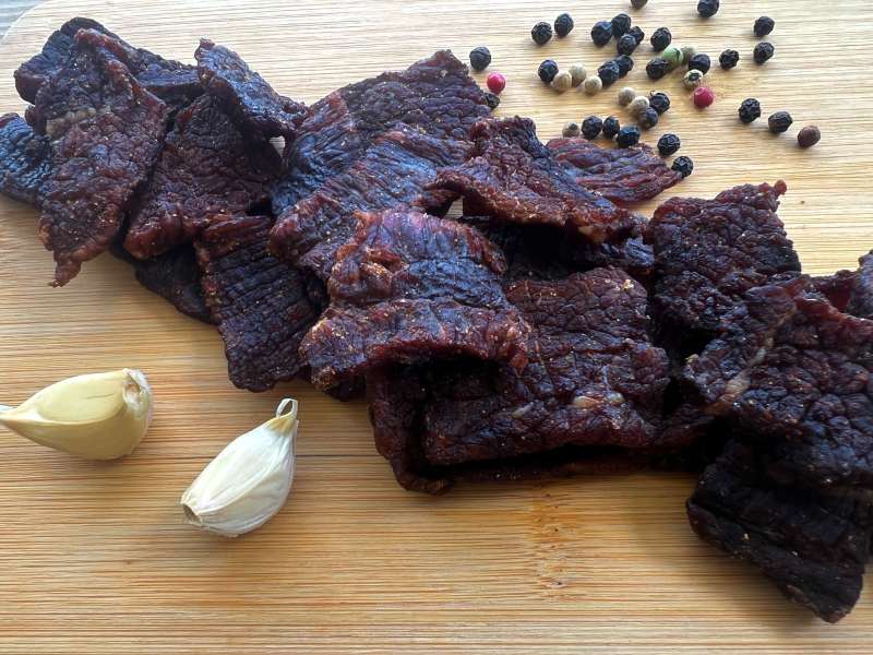 Homemade jerky pieces with garlic cloves and black peppercorns