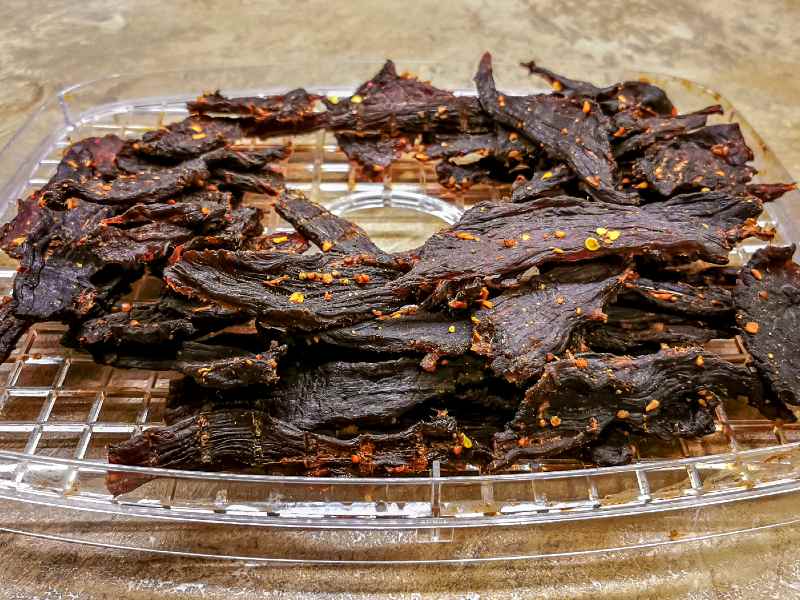 Seasoned jerky strips on a round drying rack