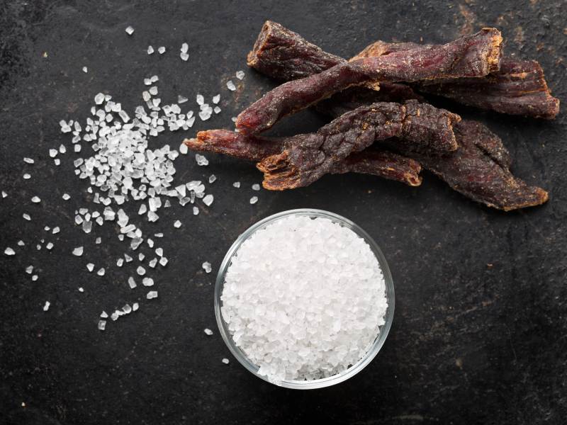 Beef jerky strips beside a small bowl of salt