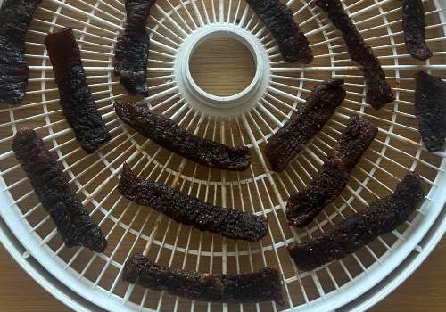 Dark Cajun jerky strips on a dehydrator tray
