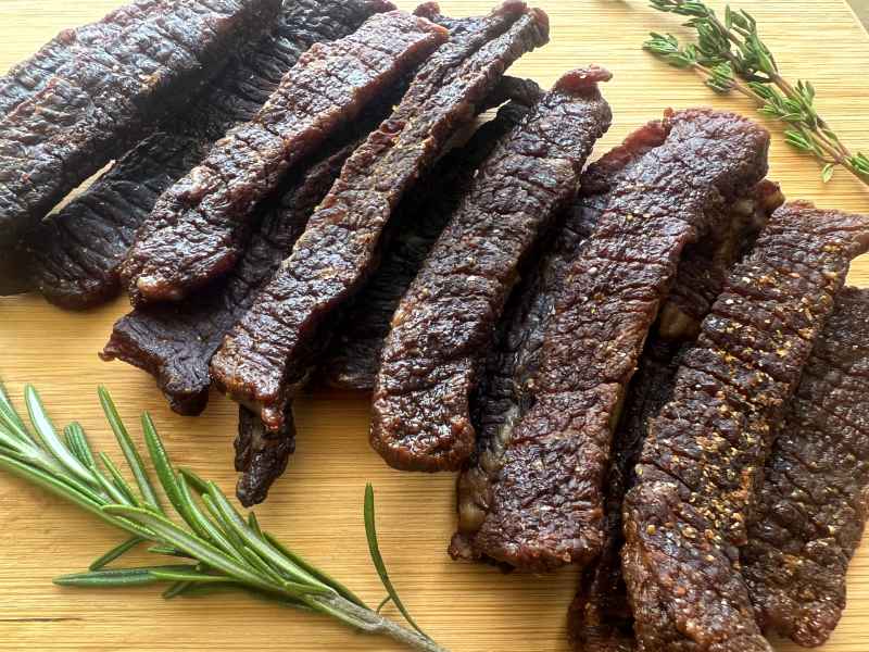 Long Cajun-style beef jerky strips beside rosemary