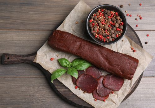 Sliced dried meat on a board beside peppercorns and herbs