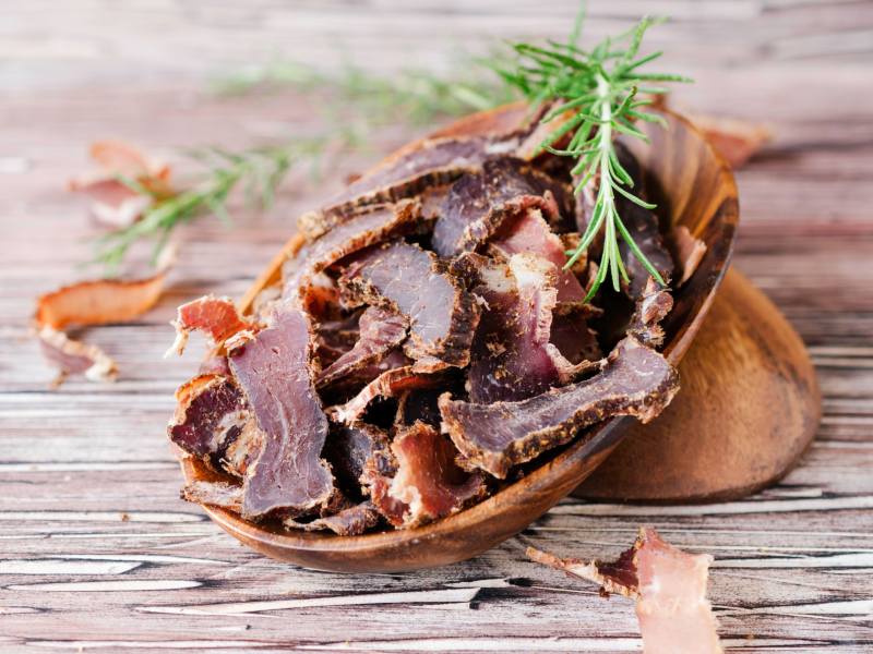 Sliced dried meat in a wooden scoop with rosemary