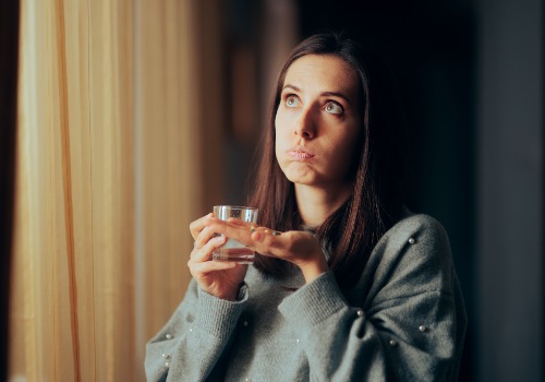 A person holding a glass of water beside a window