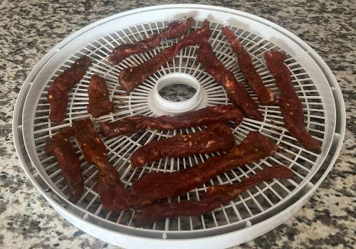 Long chili garlic beef strips laid on a dehydrator tray