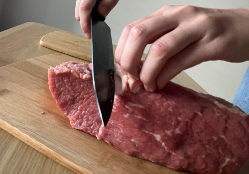 A knife trimming a pale seam from a beef roast