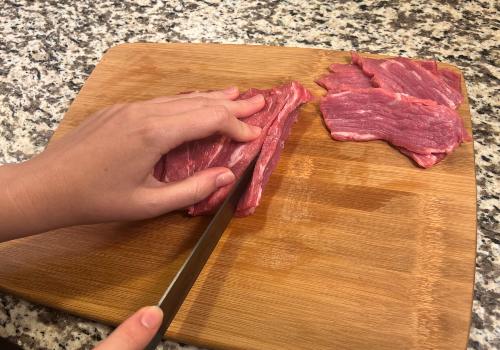 A cook slicing beef into long, narrow strips