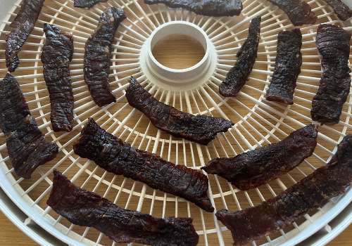 Darkened Chinese-style beef jerky on a dehydrator tray