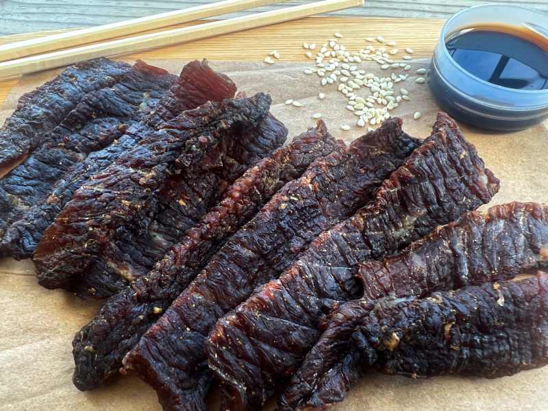 Chinese-style beef jerky beside chopsticks, sesame seeds, and a small sauce dish