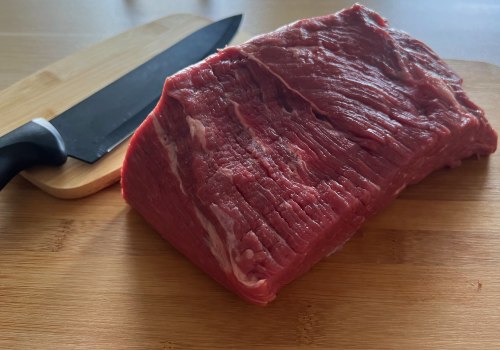 A bottom round roast beside a knife on a wooden board