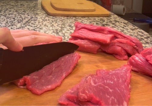 Beef being cut into thin strips on a board