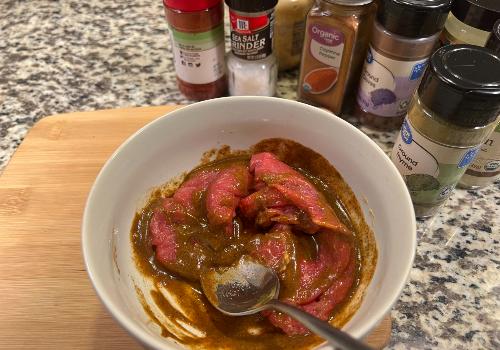 Beef strips being stirred through barbecue marinade in a bowl