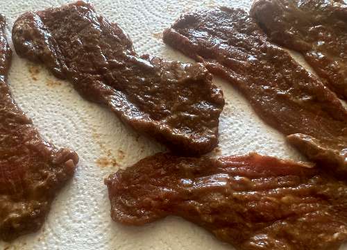 Barbecue-marinated beef strips resting on paper towels