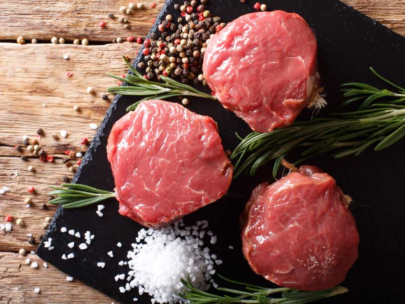 Three raw filet steaks with rosemary, peppercorns, and salt