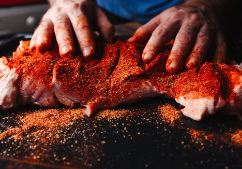 Hands spreading red spice rub over a large piece of meat