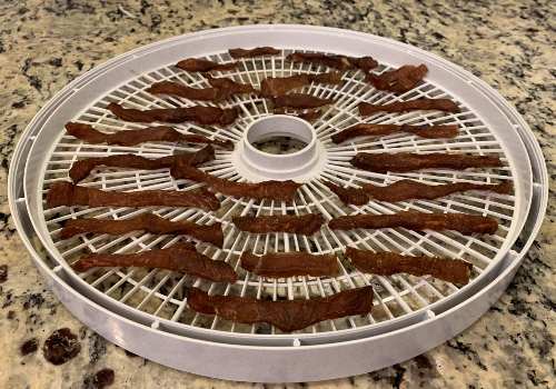 Dried pork jerky strips on a white dehydrator tray