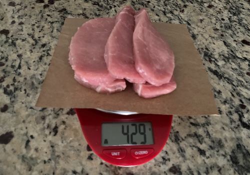 Raw pork chops on a scale reading 429 grams