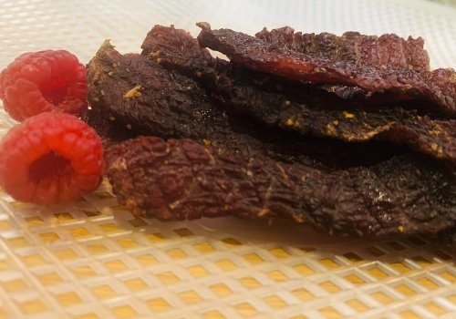 Honey-peppered beef jerky on a plate beside raspberries