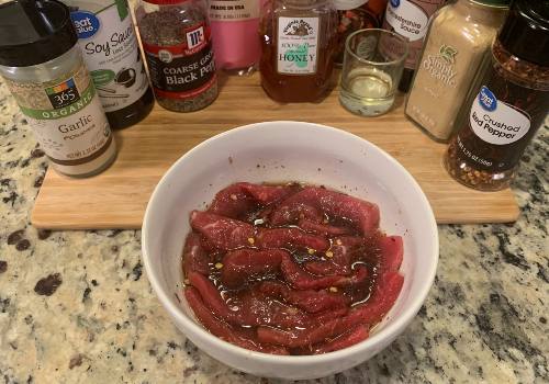Beef strips soaking in marinade with honey and spices behind them