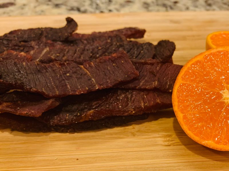 Beef jerky strips beside a halved orange