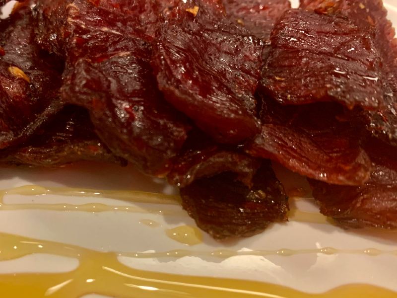 Glossy beef jerky pieces on a plate drizzled with honey