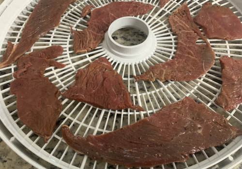 Broad marinated beef slices spread on a dehydrator tray