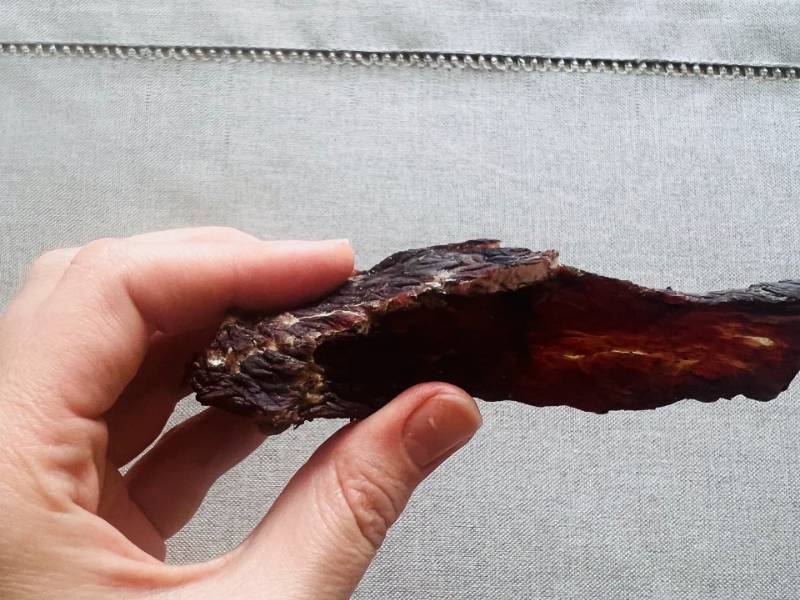 A hand bending a dark strip of beef jerky