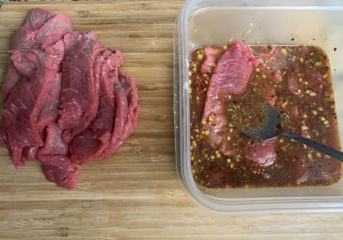Sliced beef beside a container of marinade with chopped seasonings