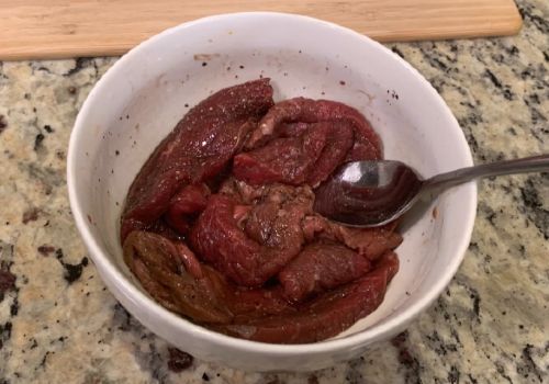 Beef strips being stirred through marinade in a white bowl