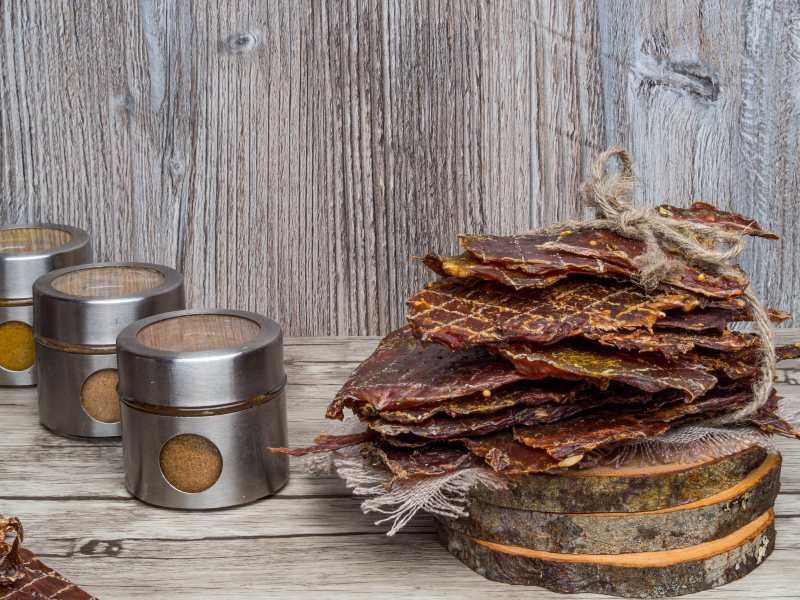 Large jerky sheets stacked on wooden rounds beside spice tins