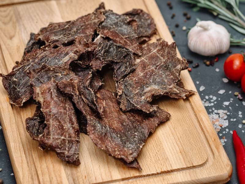 Thin dried meat slices on a wooden board with garlic and tomato