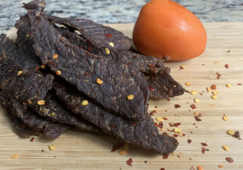 Pepper-speckled jerky strips beside a tomato half